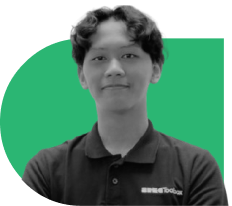 Portrait of a person with short curly hair wearing a dark polo shirt, standing in front of a green curved backdrop, facing the camera.